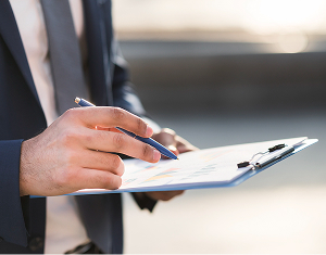 Close-up of a businessman in a suit holding a clipboard and pointing to a chart with a pen.