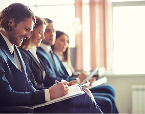 A row of business professionals taking notes on clipboards during a corporate training seminar.