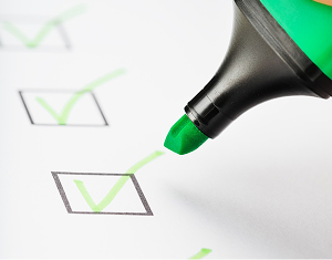 Close-up of a green highlighter pen marking a checkmark in a checkbox on a paper checklist.