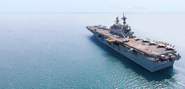 A large military aircraft carrier with fighter jets on its flight deck, sailing on a calm, open ocean.