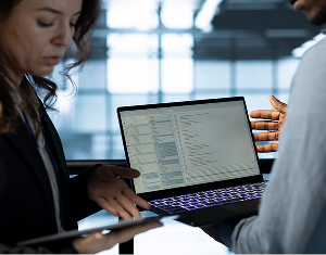 Two software developers collaborating in an office, looking at lines of code on a laptop screen.
