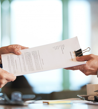A professional hands over the paperwork for a training solutions contract vehicle in a business setting.