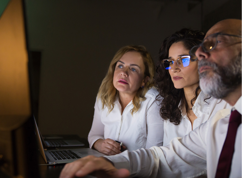 Three professionals intently view a computer screen, focused on a Cyber Security Track.