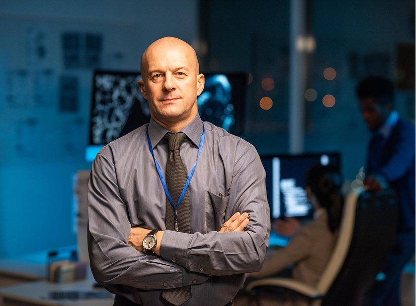 Confident IT leader with crossed arms in a tech office, representing the IT Leadership Track.