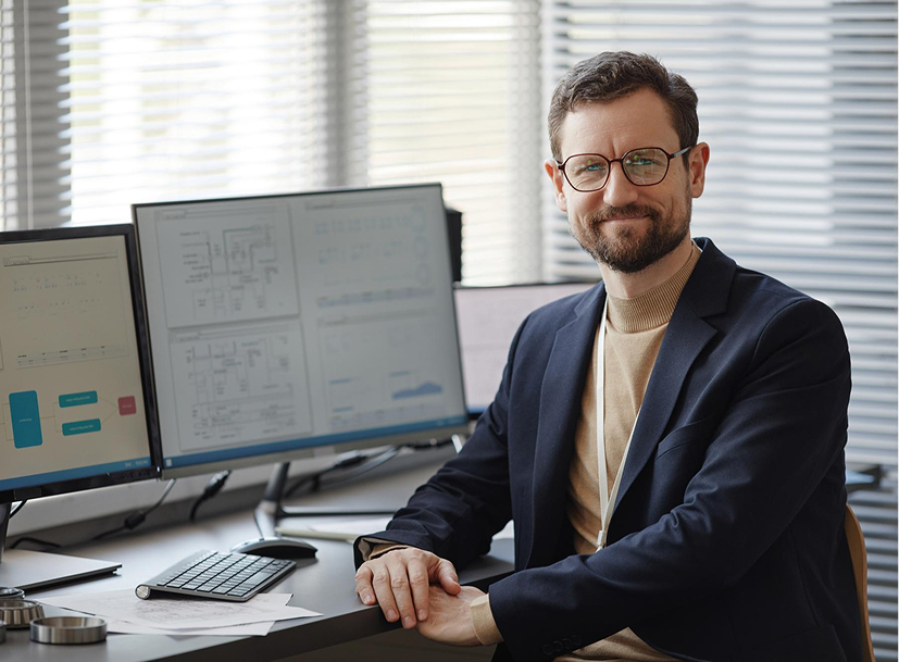 Smiling IT leader at his multi-monitor desk, an ideal visual for the IT Leadership Track.