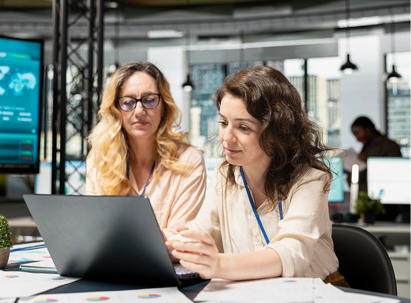 Two women review data on a laptop, demonstrating collaboration in an IT Leadership Track.