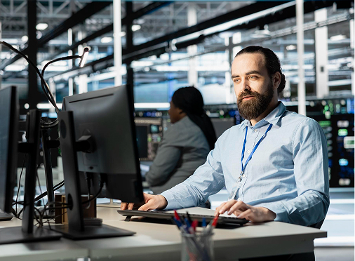Bearded man in light blue shirt focused on computer work, illustrating a professional career track.