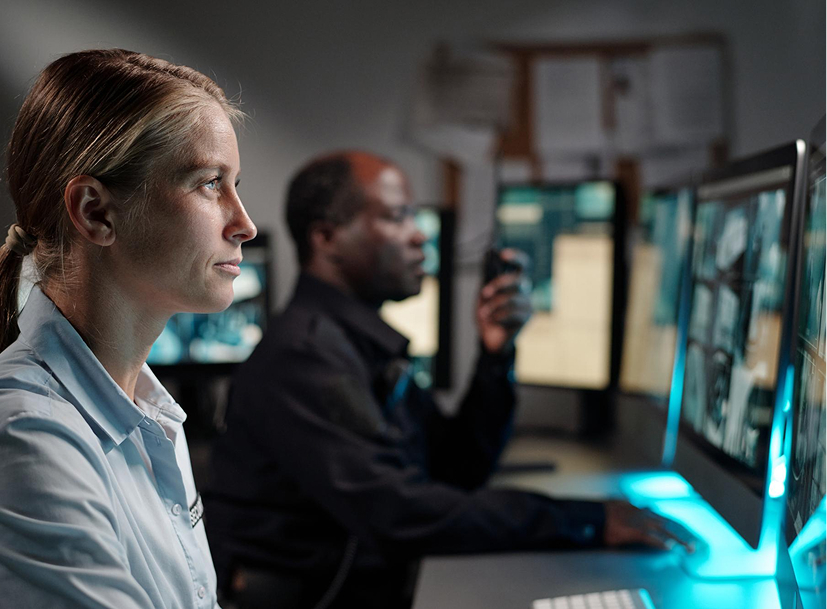 Two cyber security professionals vigilantly monitor multiple screens in a control room for a Cyber Security Track.